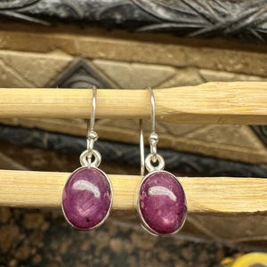 Może przedstawiać: Para srebrnych kolczyków z owalnymi, fioletowymi kamieniami szlachetnymi.