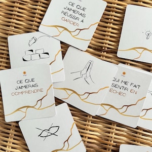 Può includere: Carte quadrate bianche con dettagli dorati e testo in francese. Ogni carta presenta un'illustrazione e una frase diversa, come un gesto della mano o le parole "Cosa vorrei capire".
