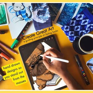 Overhead view of an artist's desk showing the creative process for Styling Socks. An iPad displays a hand-drawn Griffon dog illustration, surrounded by Posca markers, colored pencils, and watercolor paintings, emphasizing unique, hand-drawn designs.