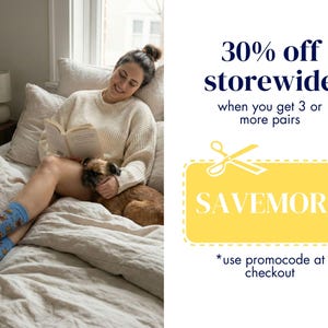 A promotional graphic showing a woman cozy in bed reading a book, wearing the blue and yellow Griffon reading socks next to a real Brussels Griffon dog. Text indicates a 30% off storewide sale when buying 3 or more pairs using code SAVEMORE.