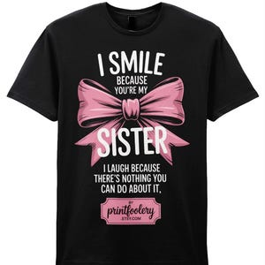 May include: Black t-shirt with the text "I SMILE BECAUSE YOU'RE MY SISTER" above a pink bow graphic. Below the bow, the text continues "I LAUGH BECAUSE THERE'S NOTHING YOU CAN DO ABOUT IT." The Etsy shop name is also included.