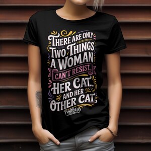 A person wearing a black graphic t-shirt with cat humour lettering against a dark wood slat background.