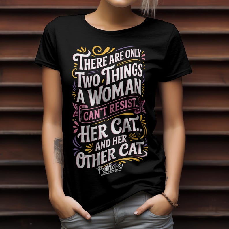 A person wearing a black graphic t-shirt with cat humour lettering against a dark wood slat background.