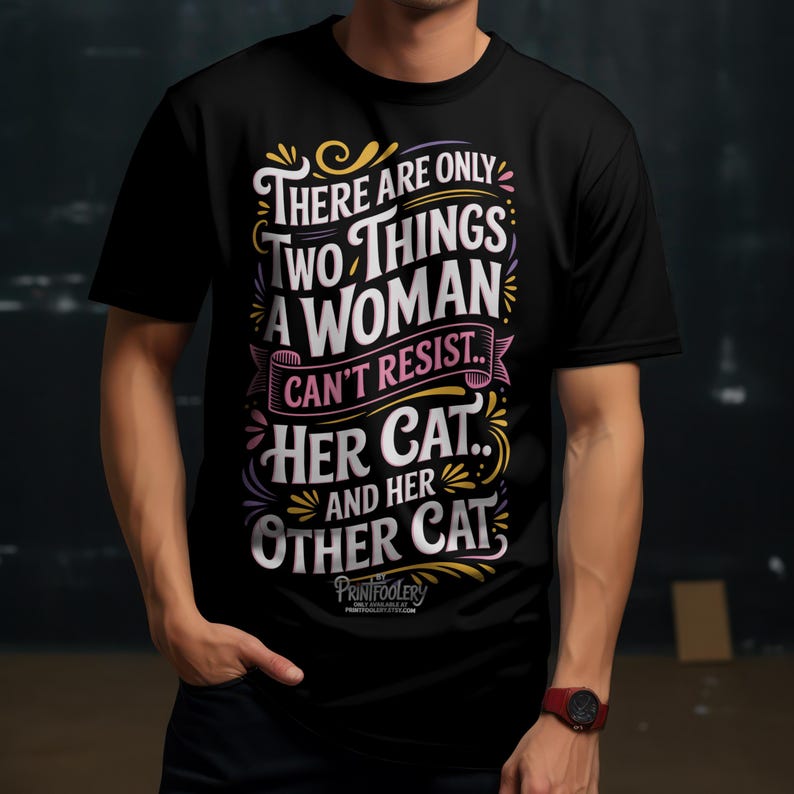 A man wearing a black t-shirt with a colourful cat design and a red wristwatch.