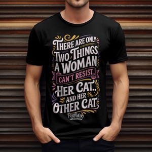 A man wearing a black t-shirt with a humorous cat typography design against a rustic wooden background.