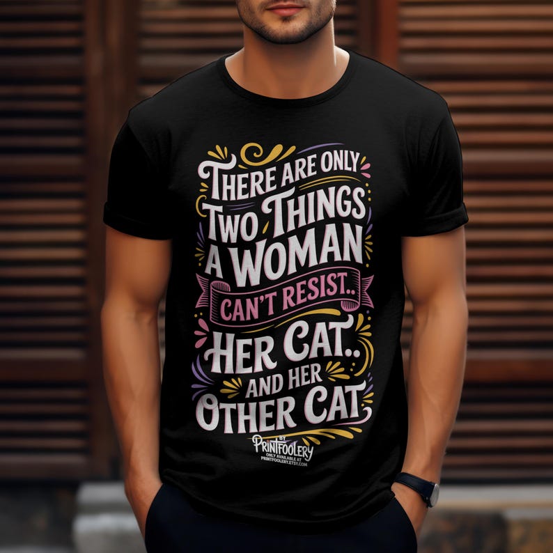 A man wearing a black short-sleeved t-shirt with cat lover text graphic against a wooden slat background.