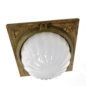 May include: A square brass ceiling light fixture featuring a central circular opening with a hinged mechanism. The fixture holds a white, ribbed, dome-shaped glass shade with a radial pattern that extends from the center to the outer edge.