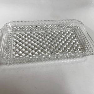 May include: A rectangular clear glass serving tray featuring a textured diamond pattern across the base and sides. The tray has integrated handles on both ends and a scalloped edge design, providing a decorative surface for serving items.