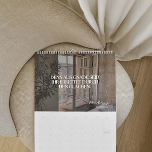 May include: A calendar with a photograph of a window and text in German, "DENN AUS GNADE SEID IHR ERRETTET DURCH DEN GLAUBEN." The calendar is open to March 3rd. The calendar is on a beige chair with a white curtain in the background.
