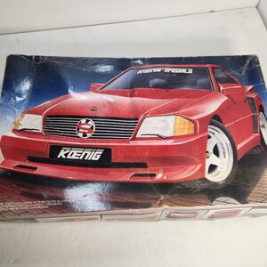 May include: A red Koenig Specials model car kit box. The box features a red sports car with white rims and the Koenig logo. The background has a blue and white gradient. The box is slightly worn.