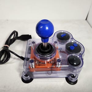 May include: A clear plastic joystick with a blue ball top and orange base. The joystick has four buttons, two of which are blue and two are black. The joystick is connected to a black cord.