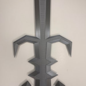 May include: A 3D printed gray sword with a sharp point and intricate details. The sword has a decorative design with a pointed tip and a series of sharp edges.