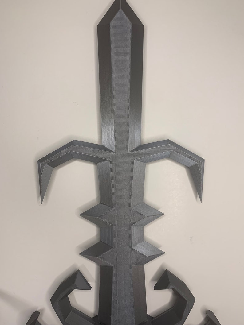 May include: A 3D printed gray sword with a sharp point and intricate details. The sword has a decorative design with a pointed tip and a series of sharp edges.