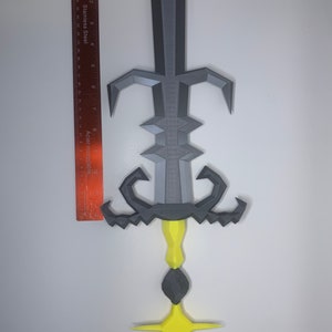 May include: A gray and yellow 3D printed sword with a star-shaped base. The sword has a detailed design with a pointed tip and a curved handle.