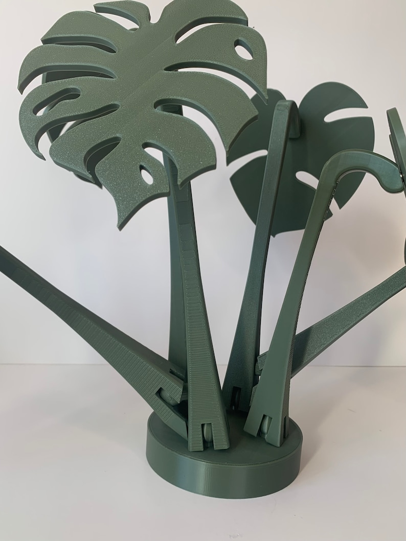 May include: A green 3D printed sculpture of a monstera plant with multiple leaves. The sculpture is made of multiple pieces that are connected together.