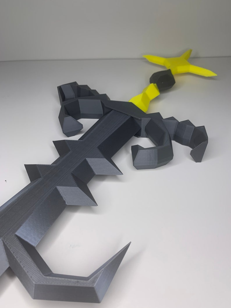 May include: A 3D printed black and yellow scorpion with a curved tail and a stinger. The scorpion is posed with its claws raised.