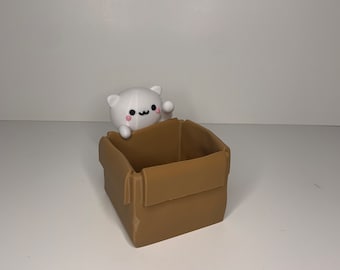May include: A white cat figurine peeking out of a brown cardboard box.