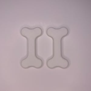 Op de afbeelding: Twee witte, botvormige objecten worden getoond tegen een witte achtergrond. De objecten hebben een afgerond, symmetrisch ontwerp, met een centrale schacht en uitlopende uiteinden. De objecten lijken 3D-geprint te zijn.