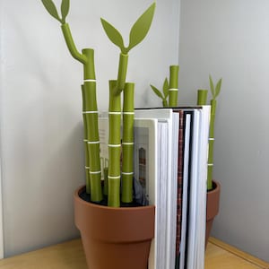May include: A brown ceramic pot with green bamboo plant bookends holding up a stack of books. The bookends are shaped like a potted plant with green leaves.