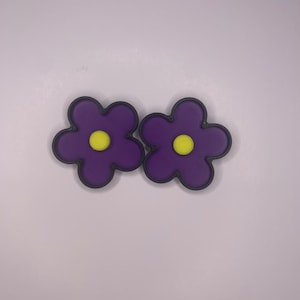 Może przedstawiać: Dwa fioletowe guziki w kształcie kwiatu z żółtym środkiem. Guziki mają czarny obrys.