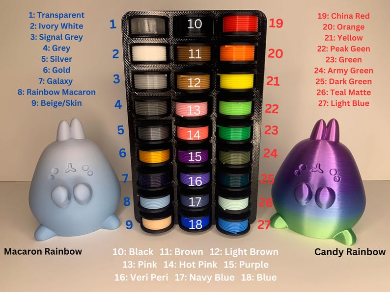 May include: A display of 27 spools of filament for 3D printing, organized in a grid with numbers 1-27. The filament colors include transparent, ivory white, signal grey, grey, silver, gold, galaxy, rainbow macaron, beige, black, brown, light brown, pink, hot pink, purple, veri peri, navy blue, blue, china red, orange, yellow, peak green, green, army green, dark green, teal matte, and light blue. The display is labeled "Macaron Rainbow" and "Candy Rainbow".