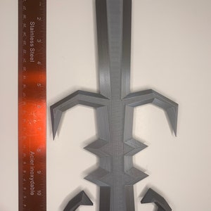 May include: A gray 3D printed sword with a sharp point and a textured surface. The sword has a decorative design with a pointed tip and a curved handle.