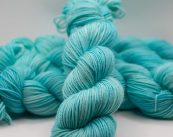 May include: Close-up of a skein of turquoise yarn. The yarn is tightly wound, showing a gradient of light and dark blue hues with white highlights. The yarn is soft and fluffy, ideal for knitting or crocheting projects.