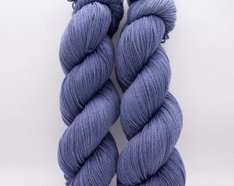 May include: Two skeins of blue yarn are displayed against a white background. The yarn is twisted into a thick, rope-like form, with a soft, textured appearance. The color is a muted, dusty blue, and the yarn appears to be made of a natural fiber.