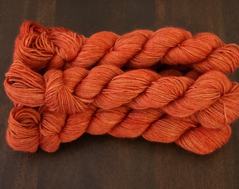 May include: Two skeins of orange yarn are displayed, showcasing a rich, warm hue. The yarn is tightly twisted, revealing subtle variations in color. The texture appears soft and inviting, perfect for knitting or crocheting projects. The yarn is a vibrant orange color.