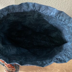 May include: A handmade tote bag with a navy blue floral patterned interior. The bag has a white rope handle and a decorative tassel at the bottom. The bag's exterior is not visible in this image.