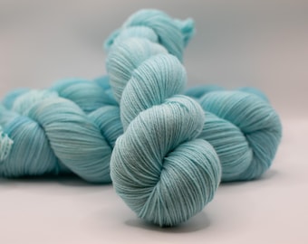 May include: A skein of light blue yarn, tightly wound and displayed against a white background. The yarn has a soft, textured appearance, suggesting it is suitable for knitting or crocheting projects. The color is a vibrant, cool tone.