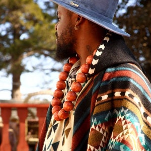 May include: A man wearing a blue hat with the word "Ravens" on it, a colorful patterned poncho, and a long necklace of wooden beads.