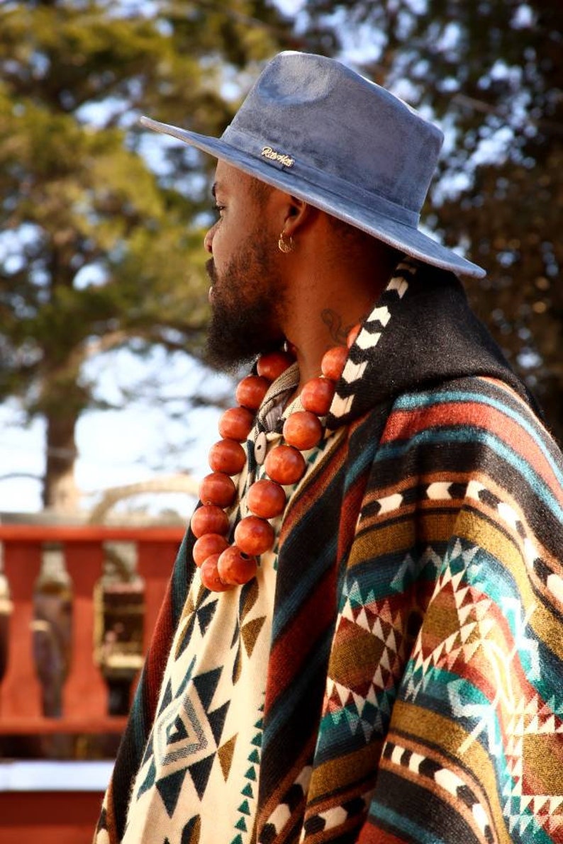 May include: A man wearing a blue hat with the word "Ravens" on it, a colorful patterned poncho, and a long necklace of wooden beads.