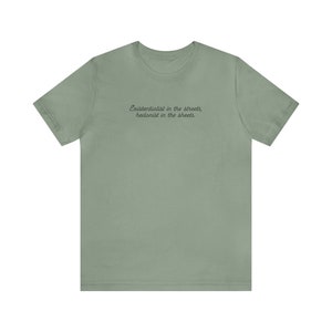 Può includere: T-shirt verde salvia con il testo "Esenzialista per le strade, edonista tra le lenzuola."
