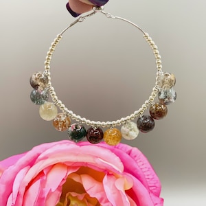 May include: Silver hoop earrings with a beaded chain and dangling gemstone beads in shades of brown, green, and white.