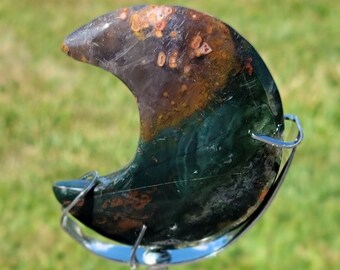 May include: A green, brown, and orange crescent moon shaped stone on a silver metal stand.