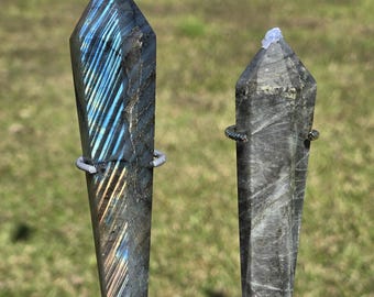 Könnte beinhalten: Zwei polierte Labradorit-Kristall-Obelisken auf Metallständern. Der Obelisk links hat blau-goldene schillernde Blitze. Der Obelisk rechts ist grau mit einer hellblauen Spitze. Die Ständer sind silber- und goldfarben.