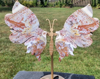 May include: A decorative butterfly sculpture with a white, pink, and brown agate wing design. The butterfly is mounted on a gold metal stand with a round base.