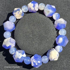 Puede incluir: Una pulsera de cuentas que alterna cuentas de ágata azul hexagonales y esféricas. Las cuentas hexagonales muestran tonos azules translúcidos con inclusiones blancas similares a nubes, mientras que las esféricas son de un azul claro semitransparente.