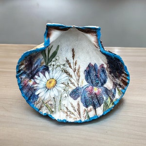 Könnte beinhalten: Eine weiße Muschel mit blauem Rand, verziert mit gemalten Blumen und Blättern. Die Muschel ist ein Dekorationsobjekt.