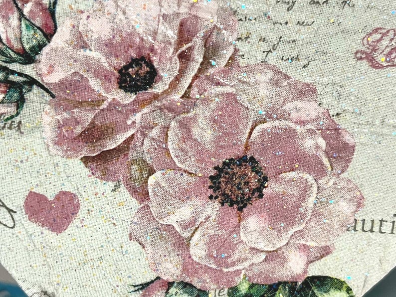 Puede incluir: Primer plano de una impresi&oacute;n floral rosa y blanca sobre un fondo de tela texturizada. Las flores tienen un aspecto delicado y descolorido y est&aacute;n acentuadas con purpurina.