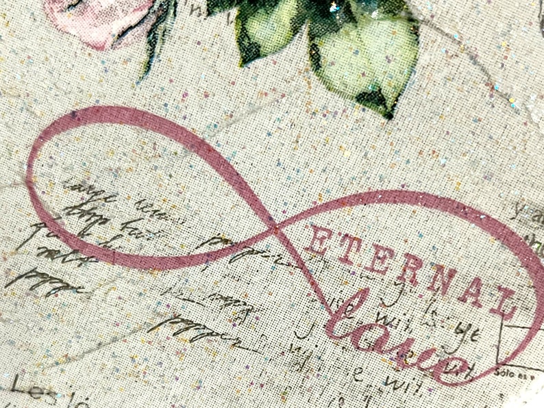 Puede incluir: Un s&iacute;mbolo de infinito rosa con la palabra "Eternal Love" impresa en negro sobre un fondo de tela beige con textura brillante.