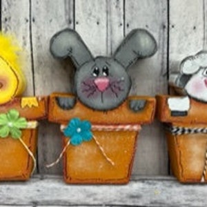 May include: Three painted wooden flower pots with animal faces peeking out of the top. The pots are brown with green, blue, and pink flowers. The animals are a yellow chick, a gray bunny, and a white sheep.