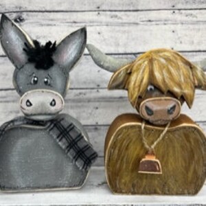 May include: Two wooden figurines, a gray donkey with a plaid scarf and a brown Highland cow with a bell around its neck.