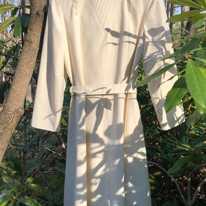 May include: A white long-sleeved dress with a high collar and a belt. The dress has a quilted design on the back.