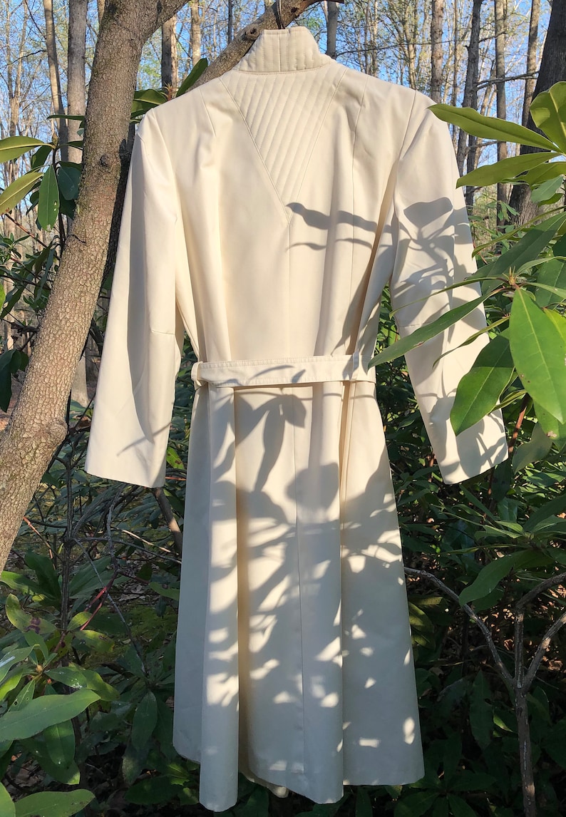 May include: A white long-sleeved dress with a high collar and a belt. The dress has a quilted design on the back.