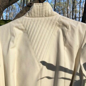 May include: A cream-colored jacket with a quilted back panel. The quilting is in a diamond pattern and the jacket has a high collar.