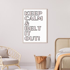 May include: A framed print with the words "KEEP CALM & BELT IT OUT!" in black outlined pink letters on a white background. The print is displayed in a room with a wicker chair, a woven basket, and a bed with an orange blanket.