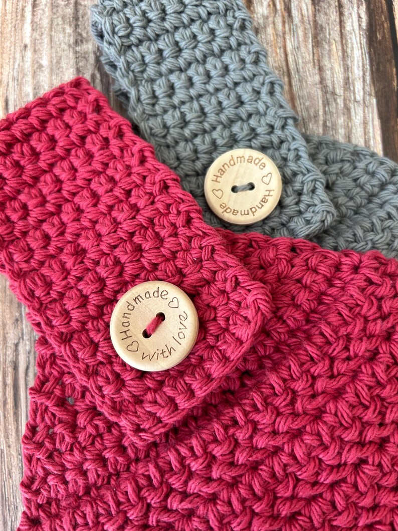 Op de afbeelding: Close-up van twee handgemaakte gehaakte hoofdbanden. E&eacute;n is fel fuchsia, de andere is grijs. Elke hoofdband heeft een houten knoop met de woorden "Handmade with love" gegraveerd. De haaksteek cre&euml;ert een textuur.