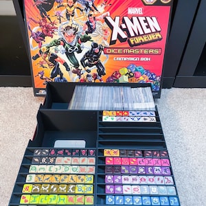 May include: A black and red box with the words "Marvel X-Men Forever Dice Masters Campaign Box" on the front. The box is open and contains a variety of colorful dice in a black plastic organizer.